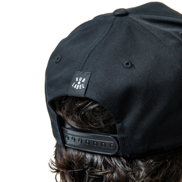 Black cap worn by a person with visible brand label on a white background