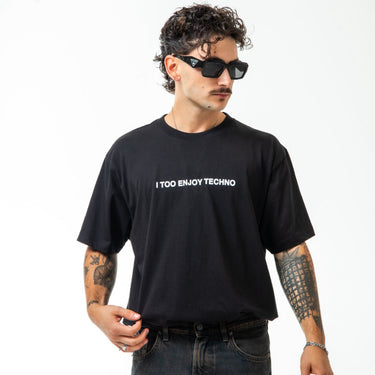 Man wearing a black t-shirt with 'I Too Enjoy Techno' text, sunglasses, and tattoos on a white background