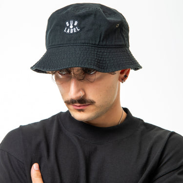 Person wearing a black bucket hat and black t-shirt with 'SUB LABEL' logo on a white background