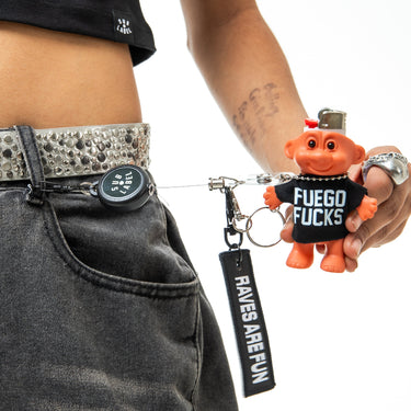 Keychain with pig figure and 'Fuego Fucks' shirt held by a person wearing a studded belt.
