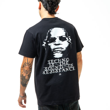 Person wearing a black t-shirt with a graphic design on the back, featuring text and a stylized face.