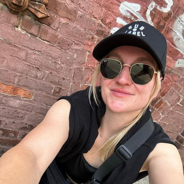 Person wearing a black cap and sunglasses in front of a brick wall