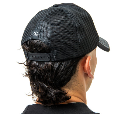Person wearing a black mesh cap with a brand logo on a white background