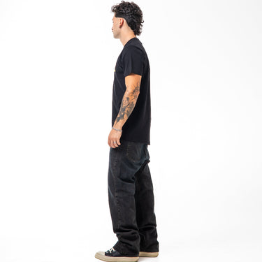 Person wearing a black t-shirt and dark jeans standing against a white background