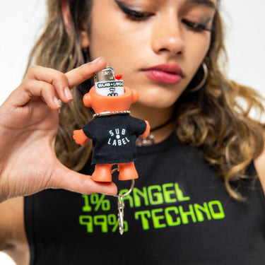 Person holding a small figurine with a black shirt labeled 'SUB LABEL' and text '1% ANGEL 99% TECHNO'.