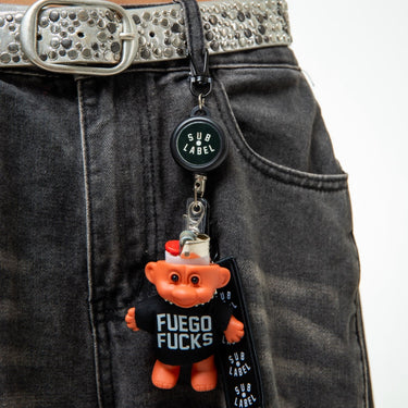 Keychain with 'Fuego Fucks' text attached to a belt on dark jeans.