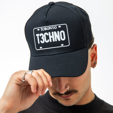 Person wearing a black cap with 'Toronto Techno' license plate design on a plain background